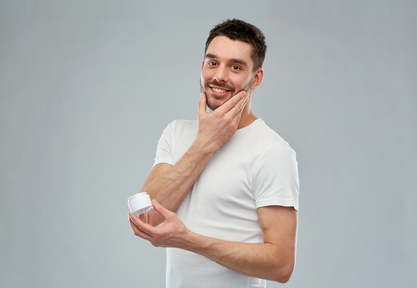 happy young man applying cream to face over gray - Foto, Bild