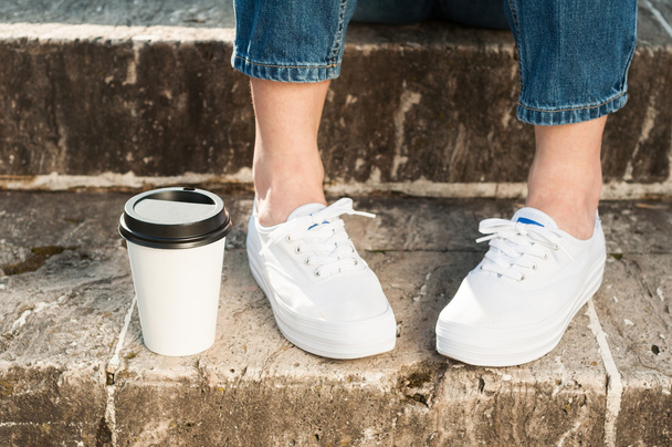 Close-up of woman wearing jeans and sneakers standing near coffe - Photo, Image