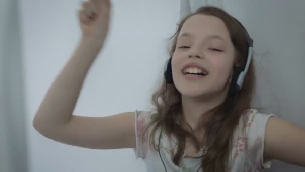 Beautiful little girl in headphones singing song emotionally and dancing - Imágenes, Vídeo