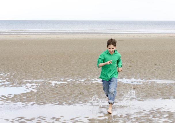 Il ragazzo con una felpa verde, correre a piedi nudi sulla spiaggia a basso
 - Foto, immagini