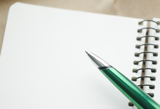 Una parte di notebook bianco aperto e penna verde sulla scrivania
 - Foto, immagini