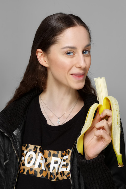 pretty girl in leather jacket bite fresh banana - Photo, Image