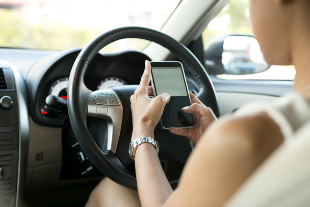 車に座っている女性は、運転中の携帯電話のテキスト メッセージを使用します。  - 写真・画像