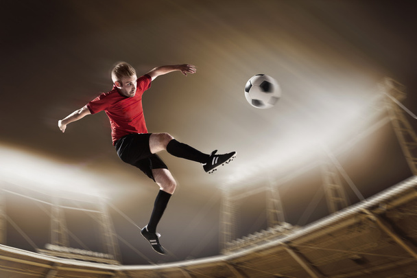 Спортсмен пинает футбольный мяч на стадионе
 - Фото, изображение