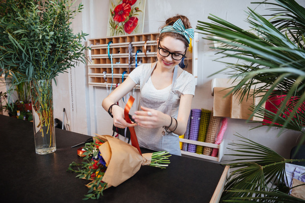 Smiling woman florist making bouquet of flowers with red ribbon - Фото, зображення
