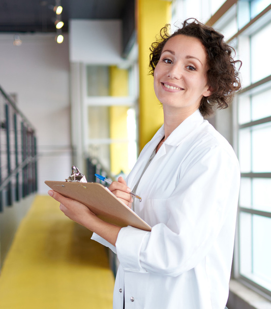 Portrait of a female doctor holding her patient chart in bright modern hospital - Φωτογραφία, εικόνα