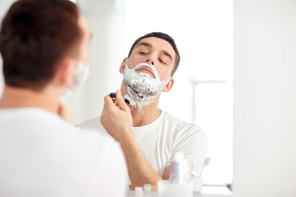 man shaving beard with razor blade at bathroom - Foto, afbeelding