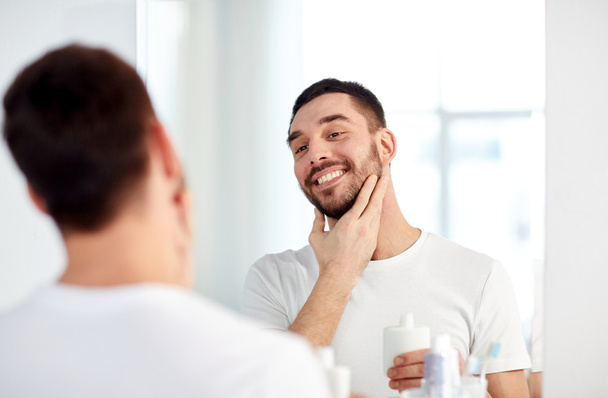 happy man applying aftershave at bathroom mirror - Foto, imagen