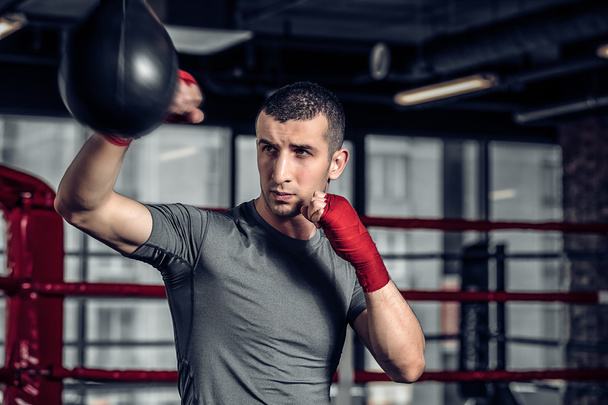 Male boxer using a punching bag in gym - Фото, зображення