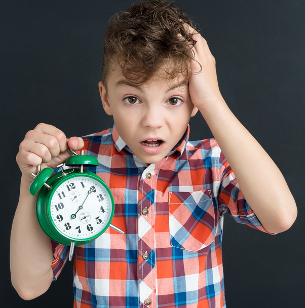 Shocked pupil with big green alarm clock - back to school concep - Foto, afbeelding