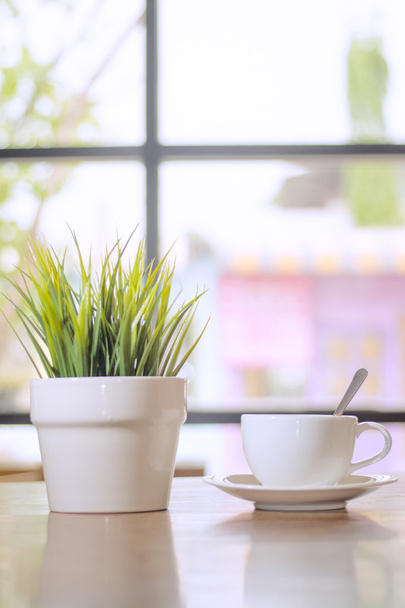 Uma pequena planta perto da janela com xícara de café
 - Foto, Imagem