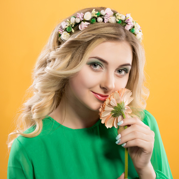  beautiful blonde girl with a wreath on his head on yellow background. Woman holds gerbera flower near the face.  - Foto, Bild