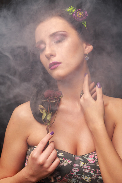 Elegante y seductora morena en una nube de humo. Morena en una hermosa corona sobre un fondo negro
. - Foto, imagen
