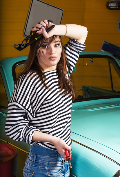 attractive  brunette woman in a striped jacket in the garage near the retro car, in the hands holding tools. - Foto, immagini
