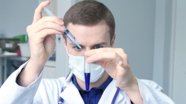 Porträt eines jungen kaukasischen Arztes, der eine Flüssigkeit aus einer Spritze in einen Schlauch gießt - Filmmaterial, Video