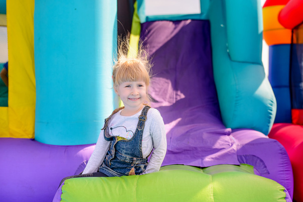 Ευτυχισμένο όμορφο μικρό ξανθό κορίτσι σε ένα φουσκωτό κάστρο - Φωτογραφία, εικόνα