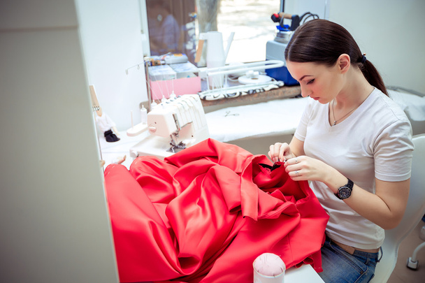 tailor sews red dress - Foto, afbeelding