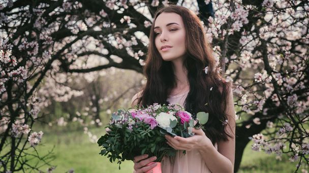 Woman in blooming trees. Woman with wedding bouquet in hands. - Photo, Image