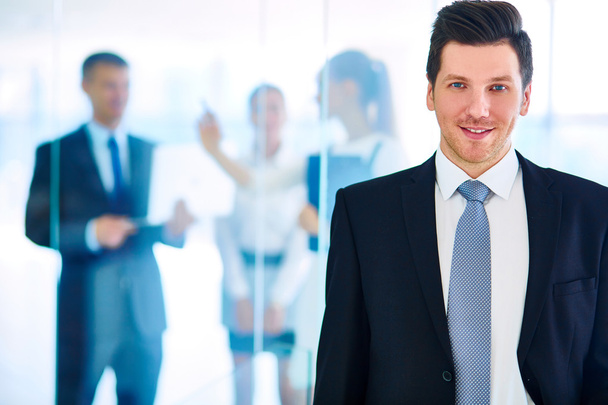 Portrait of young businessman in office with colleagues in the background - Photo, Image