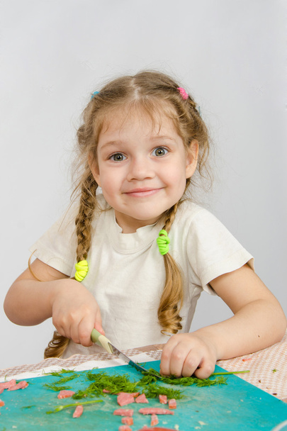 Kleines sechsjähriges Mädchen beim Schneiden des Grüns am Küchentisch - Foto, Bild