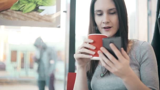 Woman using smartphone, drinking coffee in cafe. - Filmati, video