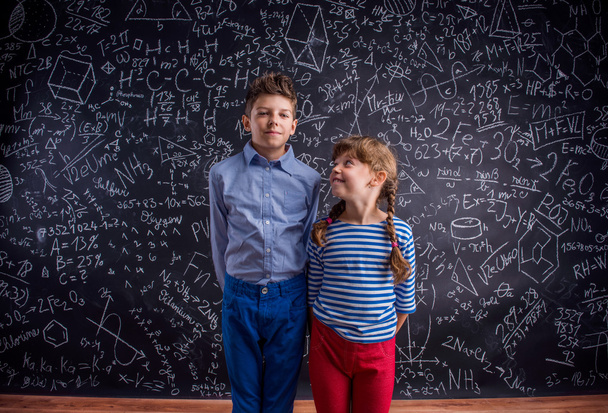 Happy boy and girl at school against big blackboard. - Φωτογραφία, εικόνα