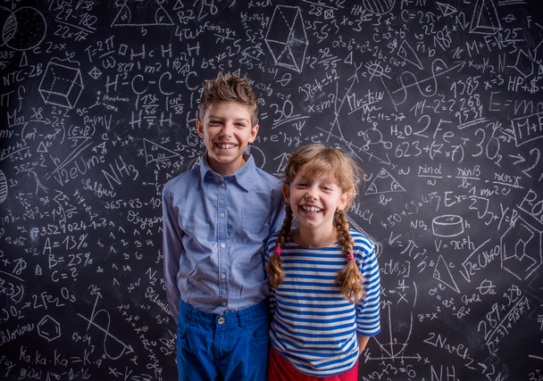 Happy boy and girl at school against big blackboard. - Foto, immagini