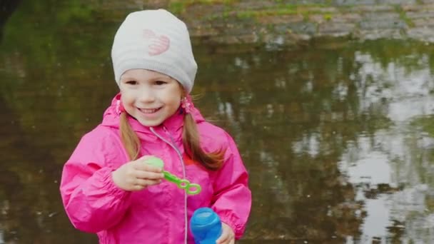 Portrait of a happy girl with soap bubbles, is on the background of a large puddle - Séquence, vidéo