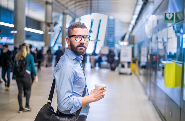 Hipster businessman holding a coffee cup, subway station - Foto, Imagen