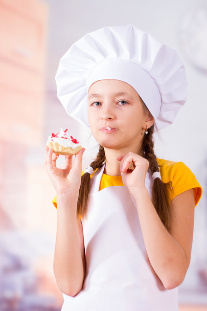 Girl in apron and cap eat delicious cookies - 写真・画像