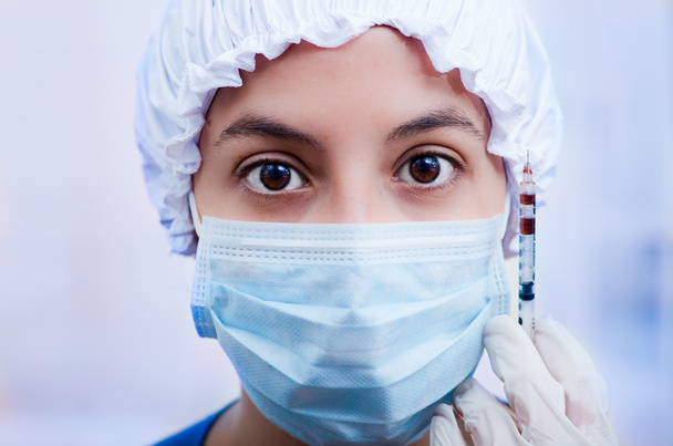 Closeup headshot nurse wearing bouffant cap and facial mask holding up syringe needle for camera - Zdjęcie, obraz