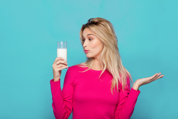 Blonde young woman a glass of milk on blue - Фото, изображение