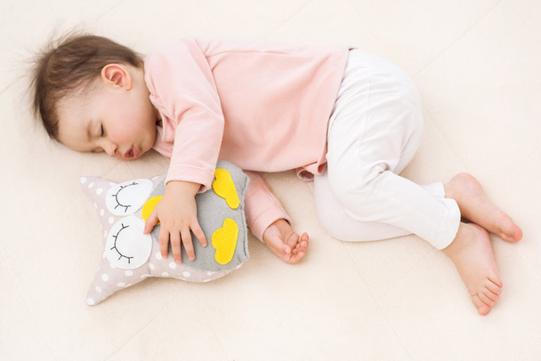 Sleeping and dreaming beautiful baby girl toddler with an owl toy on the bed - Фото, зображення