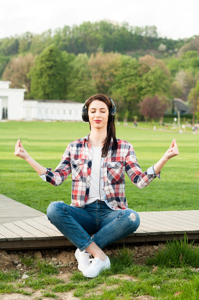 Beautiful young girl with earphones listening music and meditati - Photo, Image