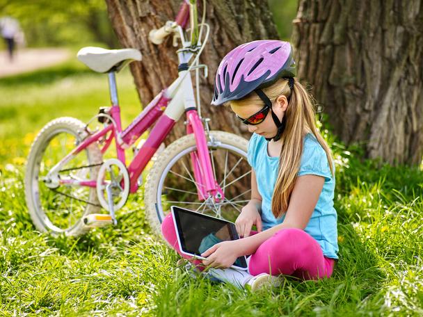 Велосипедистка в шлеме на велосипеде сидит рядом с велосипедом и смотрит планшет
. - Фото, изображение