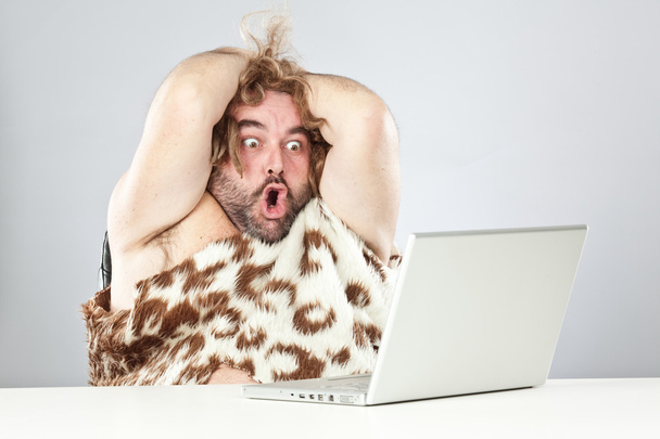 shocked funny prehistoric man using laptop - Foto, imagen