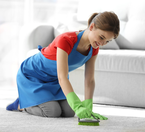 Młoda kobieta czyści dywan w pokoju - Zdjęcie, obraz