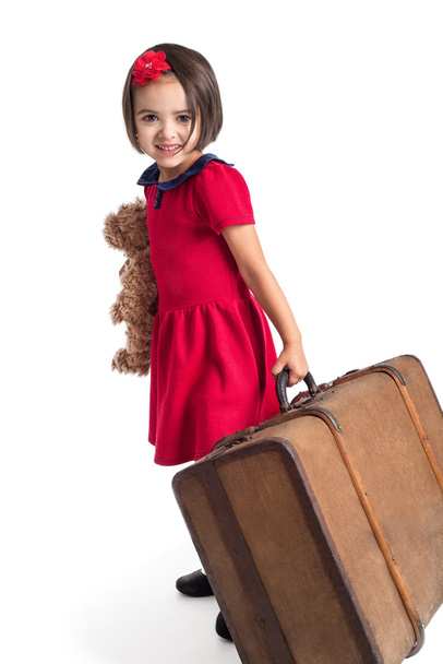 Szép kislány, mosolygós, piros ruhás, bőrönd, és a játék medve  - Fotó, kép