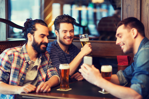 male friends with smartphone drinking beer at bar - Photo, image