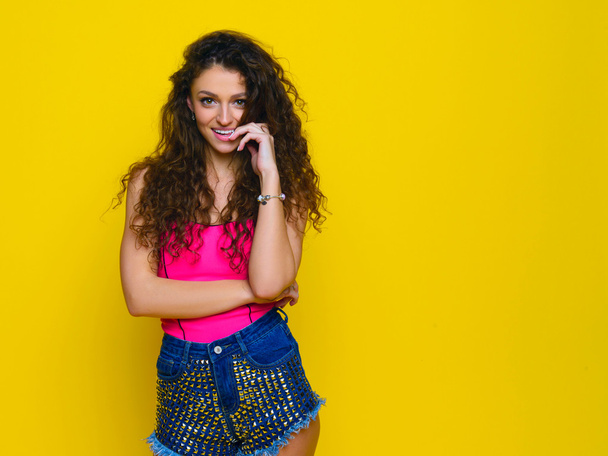 Young and beautiful curly girl in a pink shirt and blue shorts o - Фото, зображення