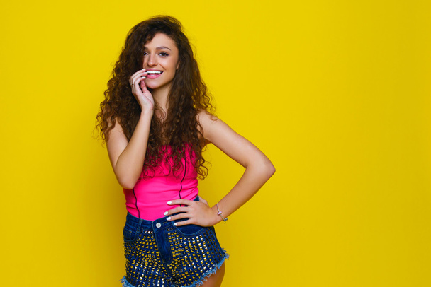 Young and beautiful curly girl in a pink shirt and blue shorts o - Фото, зображення