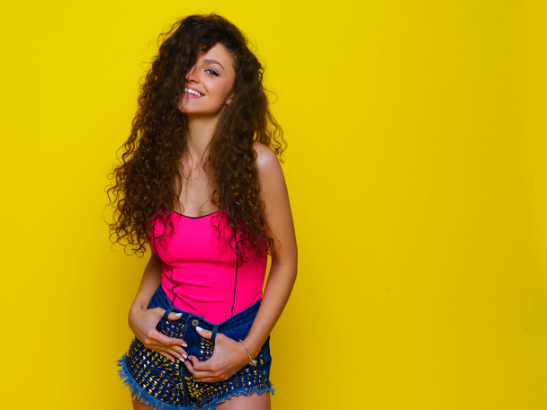 Young and beautiful curly girl in a pink shirt and blue shorts o - Foto, Imagem