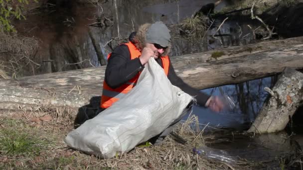 Homme avec sac ramasser bouteilles en plastique vides près de la rivière
 - Séquence, vidéo
