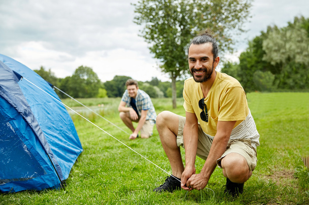 smiling friends setting up tent outdoors - Photo, Image