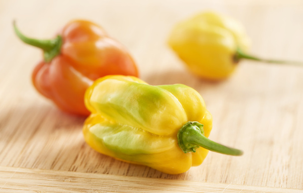 three round red, yellow and green habanero peppers on a wooden b - Photo, Image