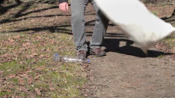 Άνθρωπος με τσάντα συλλέγει άδειο πλαστικό μπουκάλι στο δρόμο, στο πάρκο  - Πλάνα, βίντεο
