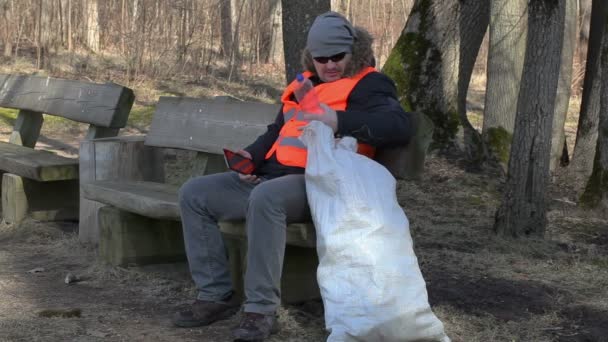 Κουρασμένος άνθρωπος με τσάντα πλαστικές φιάλες σε παγκάκι στο πάρκο  - Πλάνα, βίντεο