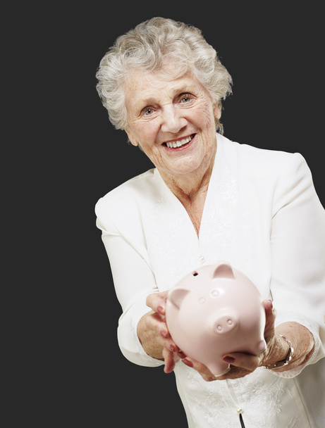 retrato de sênior mulher mostrando um porquinho banco sobre preto backgro
 - Foto, Imagem