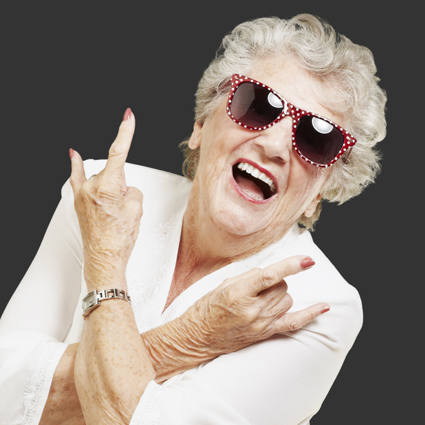 Porträt einer Seniorin, die Rock-Symbol auf schwarzem Hintergrund macht - Foto, Bild