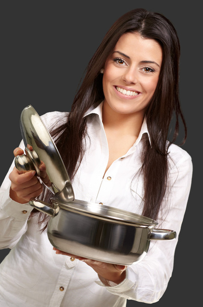 Portrait of young girl opening sauce pan over black background - Foto, afbeelding